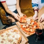 Dwie młode kobiety jedzą pizzę i piją wino w przytulnym salonie