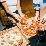Dwie młode kobiety jedzą pizzę i piją wino w przytulnym salonie